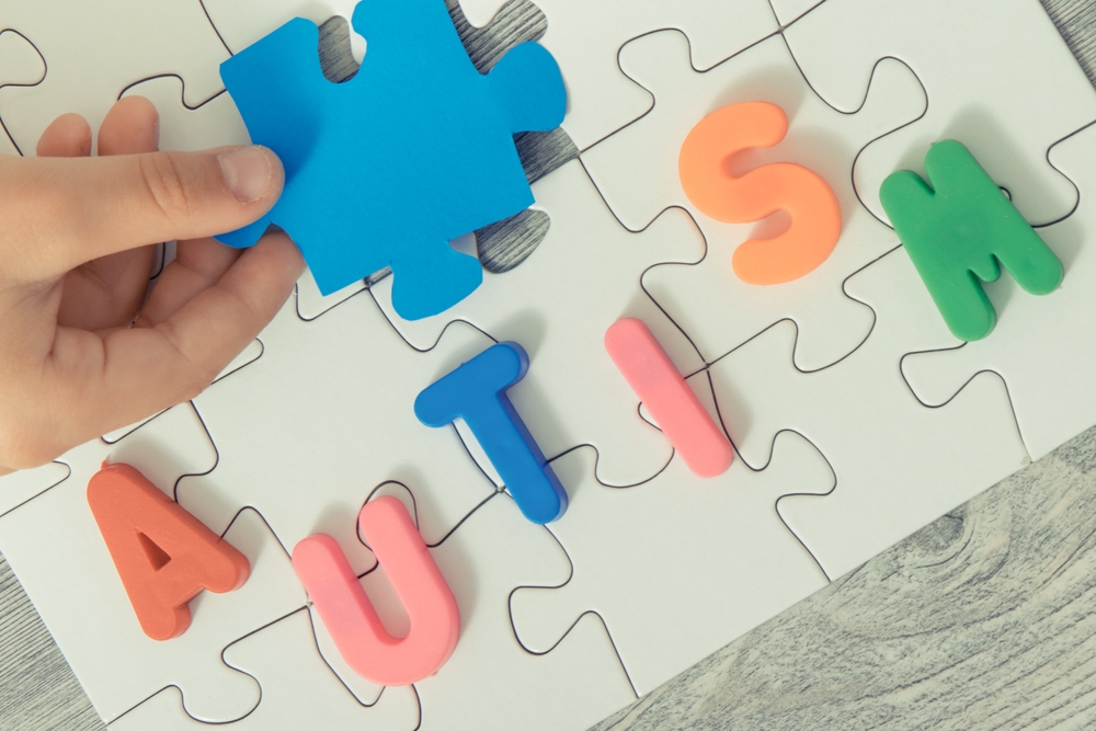 Hand of child putting together white and blue puzzle, inscription autism as symbol of Autism Spectrum Disorder. Autism Awareness Day concept