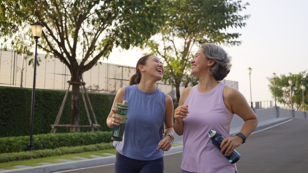 Young adult child workout outdoor public park run walk hold water bottle with mature middle age old mum. Love health care older mom asia elder people happy family protect aging fun joy city life sport