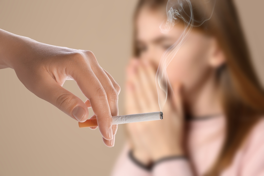 Passive smoking. Girl coughing because of woman smoking nearby on beige background. Selective focus