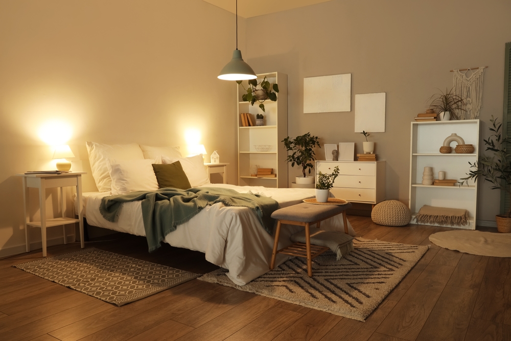 Interior of dark bedroom with cozy bed, houseplants and glowing lamps