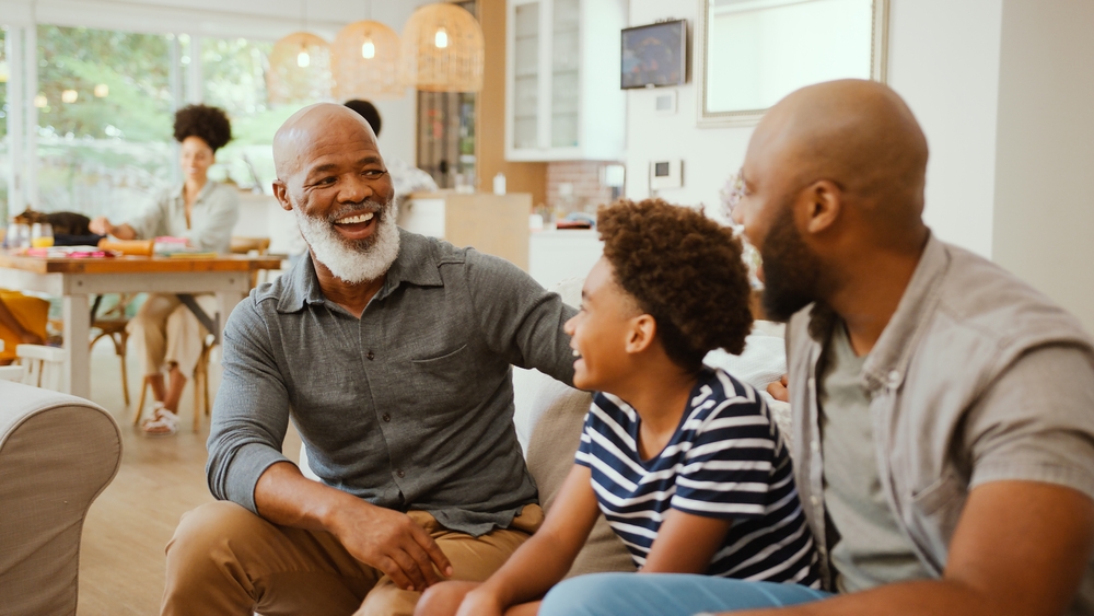 Laughing Multi-Generation Male Family Hanging Out On Sofa At Home Talking Together
