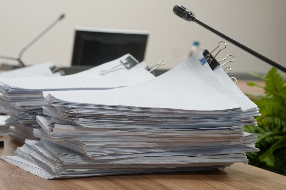 Piles of sorted business files and legislative reports on a wooden table. Closeup of heavy paperwork prepared for a government hearing or symposium. Photo