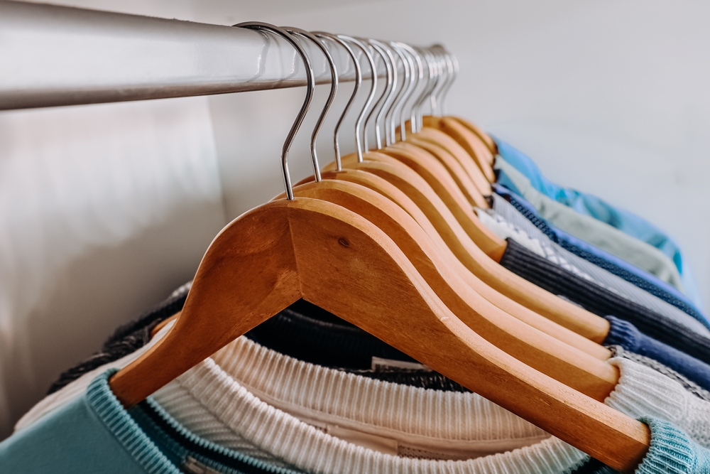 A wardrobe filled with neatly arranged shirts of various blue and teal shades on wooden hangers in an organized interior.