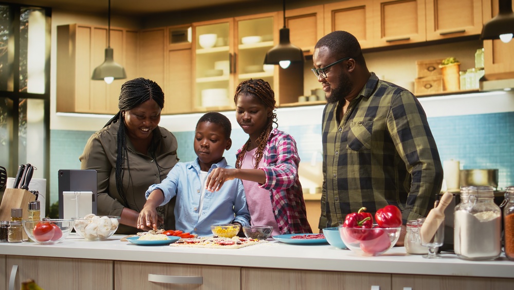 Smiling children help parents prepare pizza by sprinkling grated cheese in the kitchen, family cooking activity during the weekend. Cozy moment of teamwork and meal preparation. Camera A.