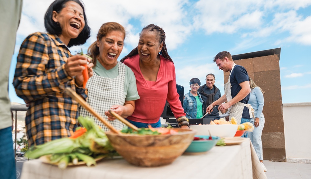 Multi generational people doing barbecue at home's rooftop - Multiracial friends having fun eating and cooking during weekend day - Summer and food concept - Main focus on man with red hair face