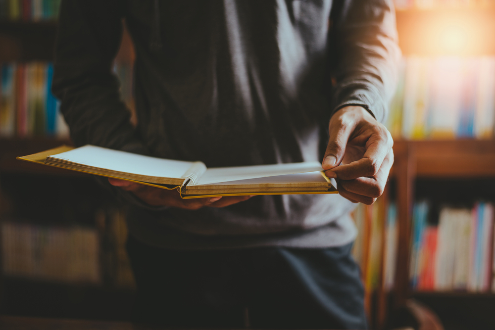 The men standing reading in the library have bookshelf are background.Read the book in a quiet place alone is a practice meditation.