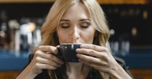 Drinking Caffeinated Coffee or Tea Could Cut Your Risk of Heart Attack and Stroke — Here's By How Much blond woman drinking coffee or tea from a dark blue mug
