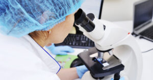 Can Biopsies Cause Cancer to Spread? Experts Explain the Risk a medic or scientist examines bacteria in a microscope against the backdrop of a bacteriological laboratory