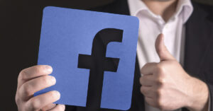 15+ Facebook Hacks You Didn’t Know You Could Use Man giving a thumbs up while holding a cardboard sign featuring the Facebook logo