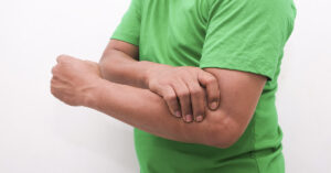 Health Expert Says Failing This Simple Body Test Could Mean a Shorter Life man in green t-shirt holding inside of elbow indicating pain or discomfort
