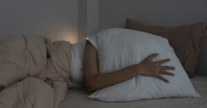 9 Foods That Might Be Ruining Your Sleep woman with pillow over her head in bed