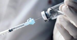 First American to Get COVID Shot Reveals What Happened Over 6 Years Close up of syringe extracting liquid from a vile. Vaccination concept