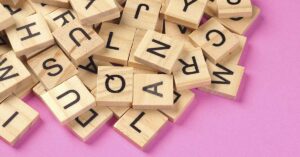 10 Words Americans Almost Always Mispronounce Wooden Scrabble pieces piled on a pink surface