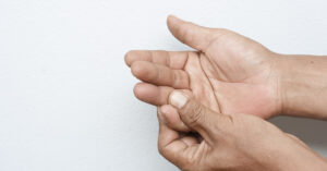 Reasons You Could Have Numbness or Tingling Sensations in Your Hand person using one hand to massage or feel the other, a gesture commonly associated with managing pain, tingling, or numbness in the hand
