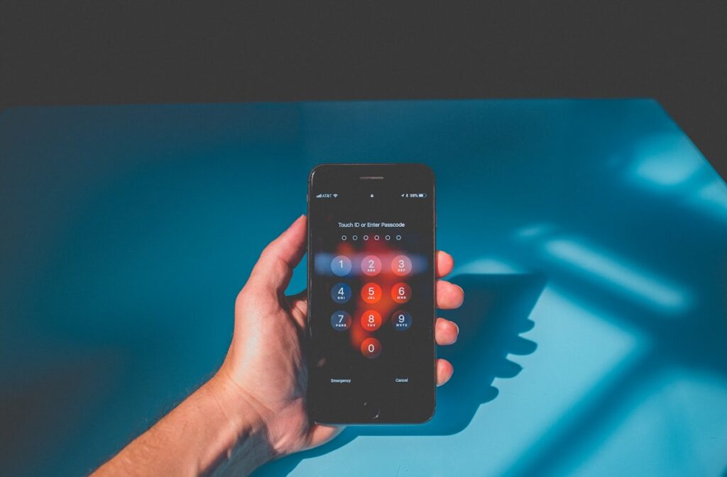 A hand holds a smartphone displaying a PIN entry lock screen, photographed against a blue surface with dramatic shadow patterns.