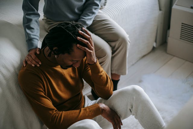 man sitting by bed, holding head