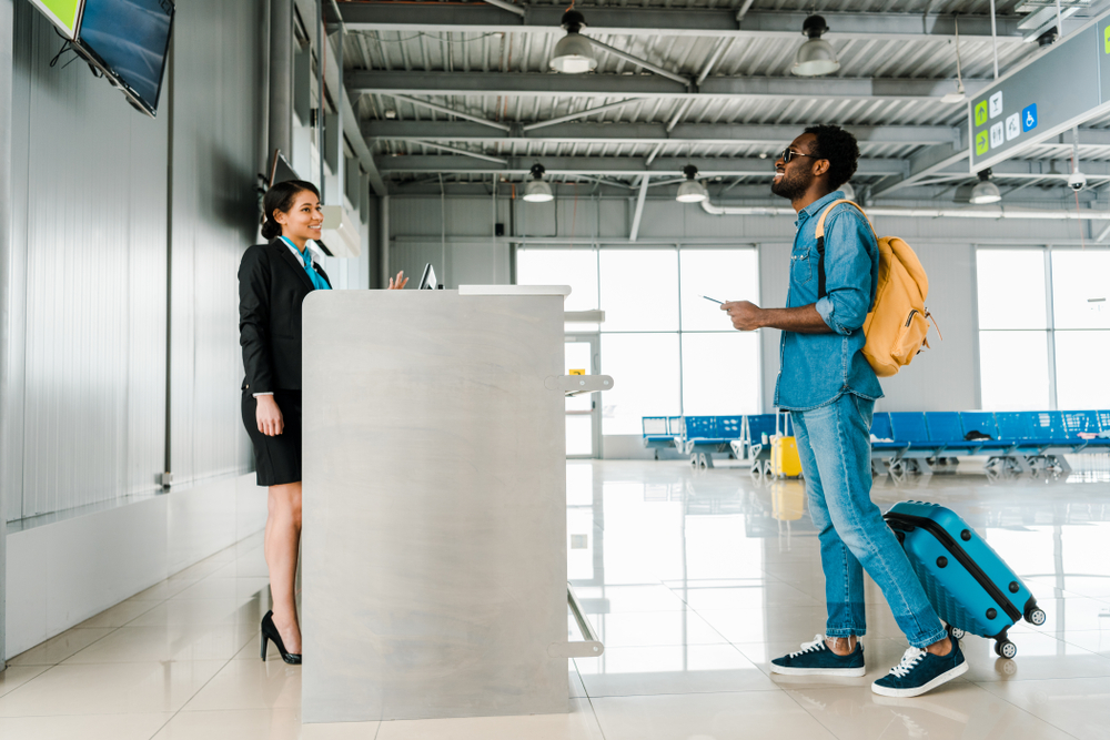 side view of smiling african american airport worker and tourist with backpack and suitcase