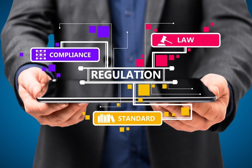 Close up of businessman hand holding pad with abstract digital regulation sketch or hologram on blue wall background. Compliance, management and law concept