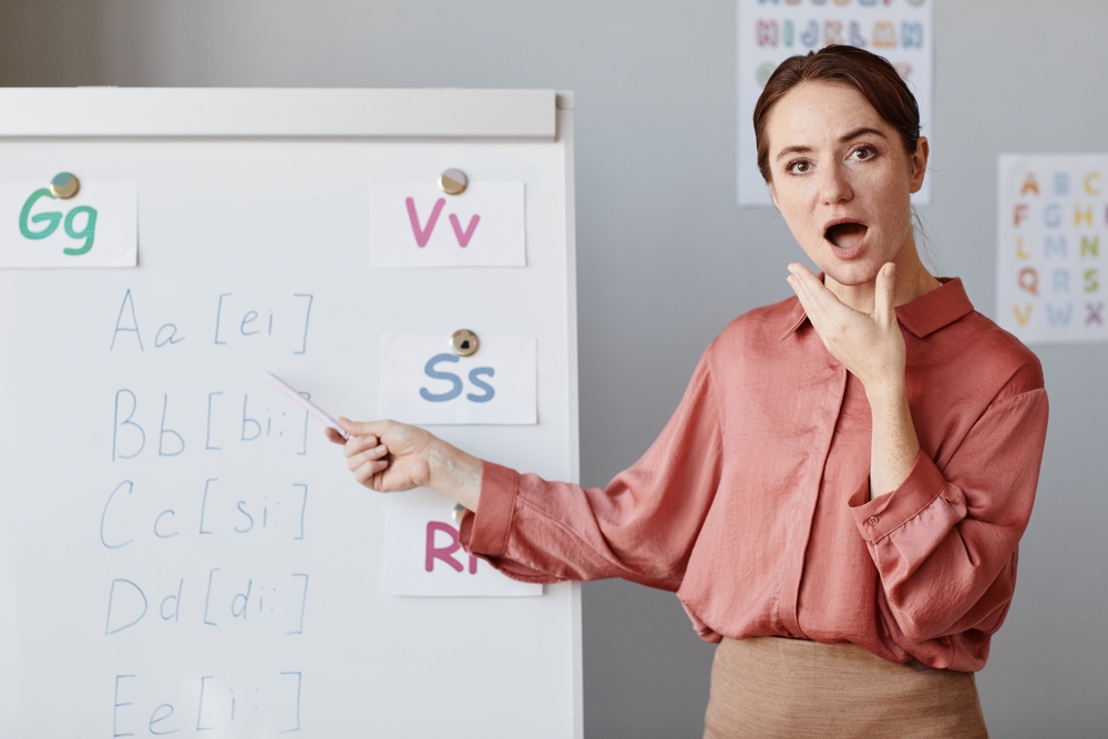 Portrait of young English teacher pointing at whiteboard with English alphabet and teaching English at school