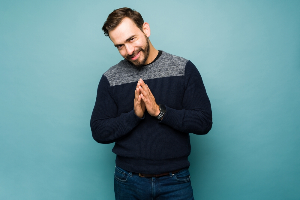 Mischievous caucasian young man making a plan and rubbing his hands together while looking happy making eye contact