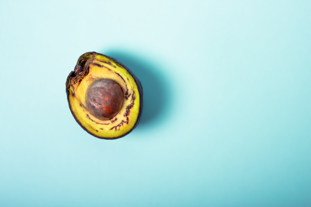 Rotten avocado, overripe, bad avocado. Fruit cut in half, free food concept, green background. The theme of careful use and care for the environment. Copy space