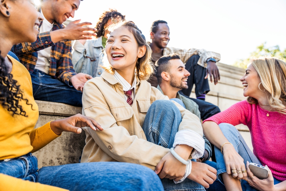 Multicultural friends having fun laughing out loud in city street - Group of young people smiling outdoors - Friendship concept with guys and girls talking and socializing hanging out together 