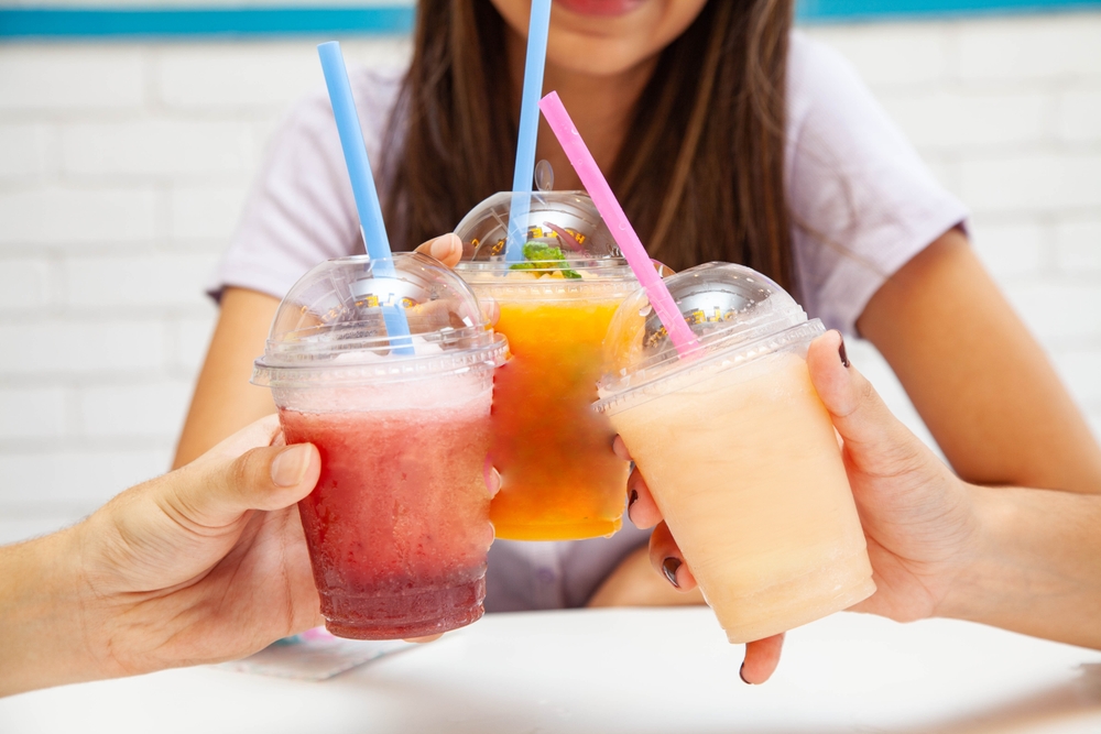 Friends holding drinking together fruity slush drinks. 