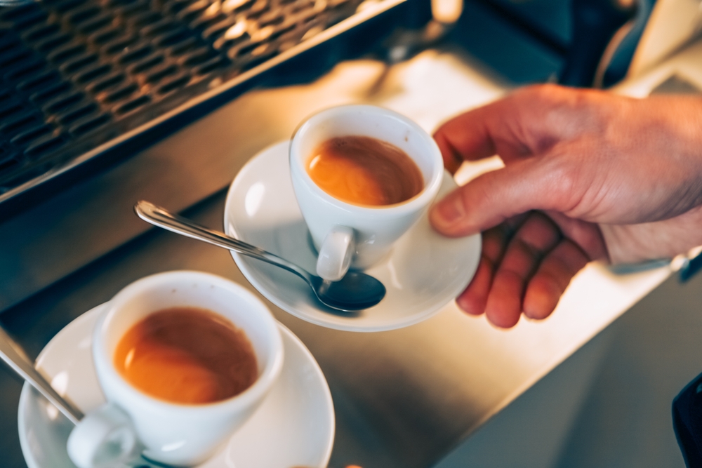 Barista holding two espresso cups on a countertop, showcasing freshly brewed coffee in a cozy café setting