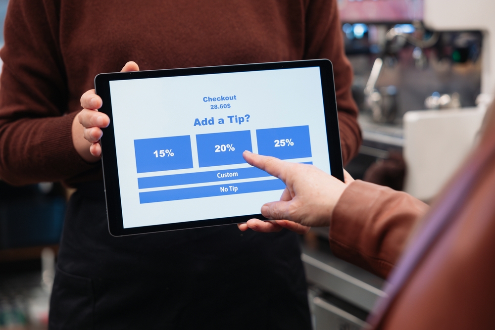 Employee holding tablet for tip payment in cafe and customer touching it to pay tip