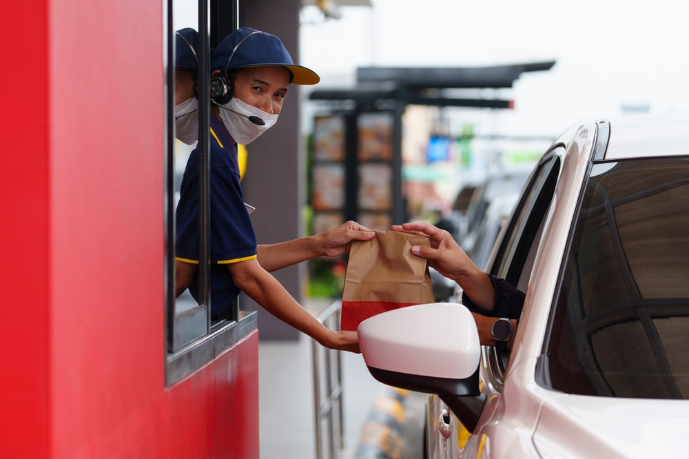 A customer picks up a burger and a soda snack in his car during rush hour from a drive-thru employee.