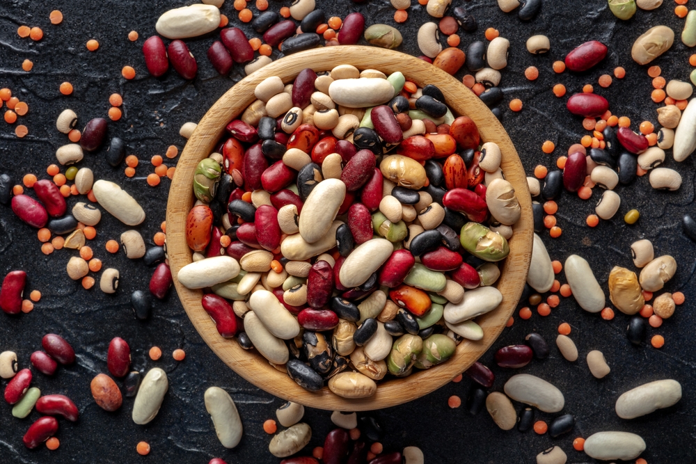 Legumes in a wooden bowl. Many different pulses, overhead flat lay shot. Various beans and grains on a black background