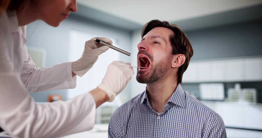 Doctor examining patient's sore throat with tongue depressor during checkup. Security camera inspection at the dentist office with female nurse