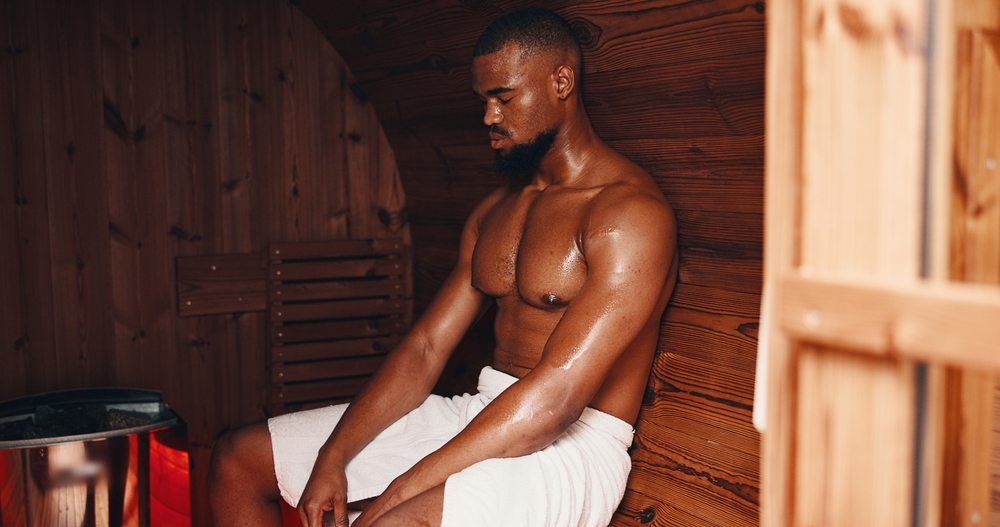 Sauna, fitness and relax with black man in gym for muscle recovery, post workout and health. Detox therapy, athlete cramp prevention and wellness with person in steam room for sweating and spa
