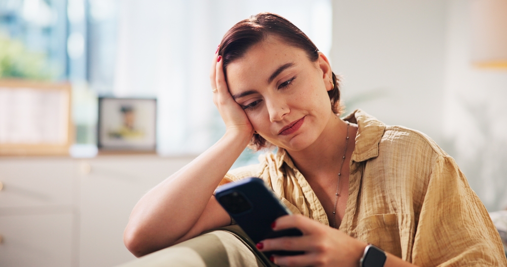 Woman, phone and bored on sofa in home, texting and check notification on web in living room. Person, smartphone and relax with chat, dating app and scroll on social media in lounge at apartment