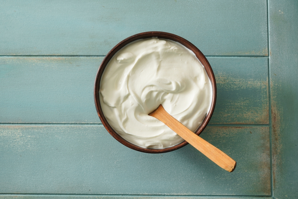 Sour cream in bowl on wooden table. Natural yogurt. Top view.