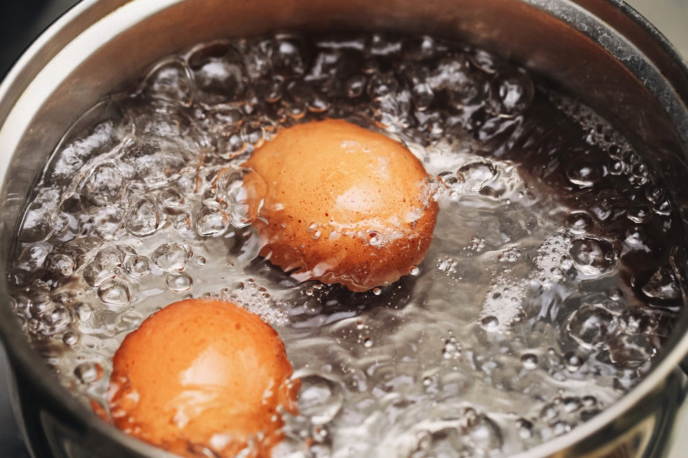Brown eggs boiling in hot water. Two whole eggs cooking in saucepan. Kitchen steam and bubbles closeup. Preparing hard boiled eggs. Healthy breakfast food concept. Boiling process in pot.