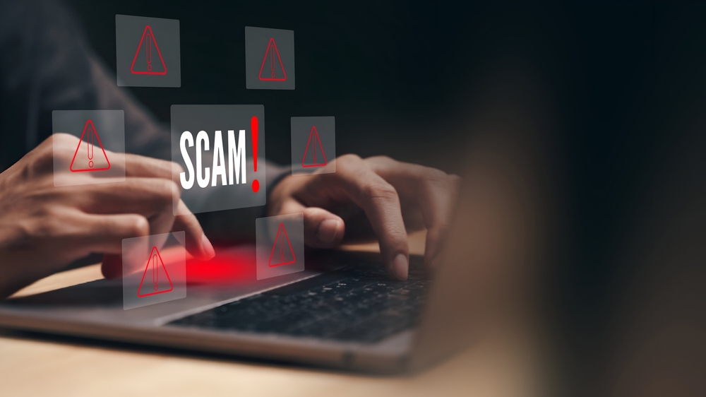 A business person using laptop with visual screen Scam Alert warning sign for scams with icons.