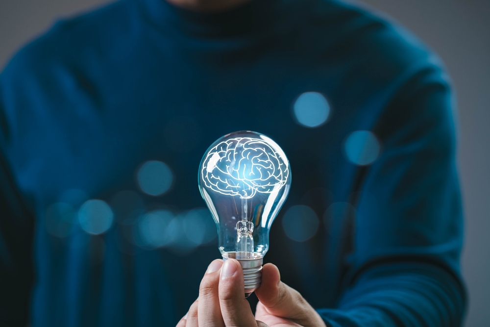 A person holds a light bulb with a brain illustration, symbolizing ideas, creativity, and innovation against a blurred background.