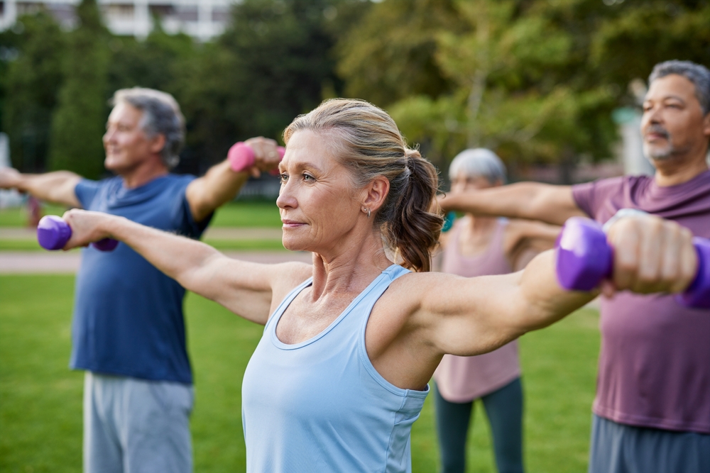 Elderly people lifting small weights at park. Focused senior woman working out with group of friends. Group of mature people doing dumbbell exercises in a park. 