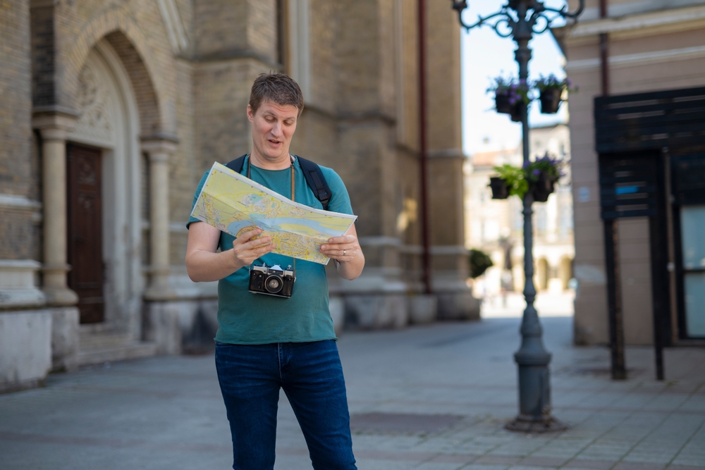 Adult man lost in a foreign city holding a paper map and a camera