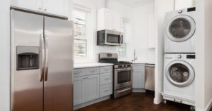 An apartment kitchen with white and grey cabinets, stainless steel appliances, and a stacked washer and dryer. No brands or names.
