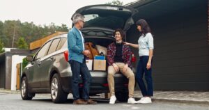 Is College Really Preparing Students for Jobs in 2026? Happy parents farewell with their son outside. People standing near grey car full of son's things and communicating with each other. Positively smiling and having good feelings before trip.
