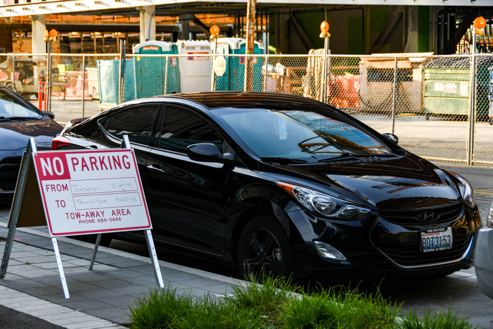 SEATTLE, WA, USA - JUNE 2018: "No parking" sign with information on restrictions. A car is parked behind the sign.