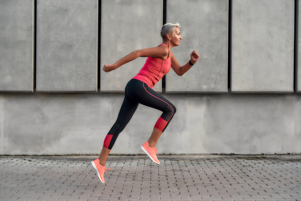Full of energy. Side view of active middle aged woman in sport clothing jumping while exercising outdoors. Healthy lifestyle concept. Sport after 50