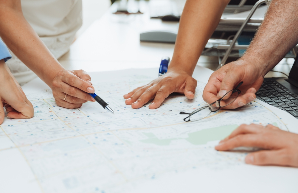 Top view of a wooden conference table with charts and graphs, papers on the table and the hands of business people folded together applauding. A concept for a business meeting.