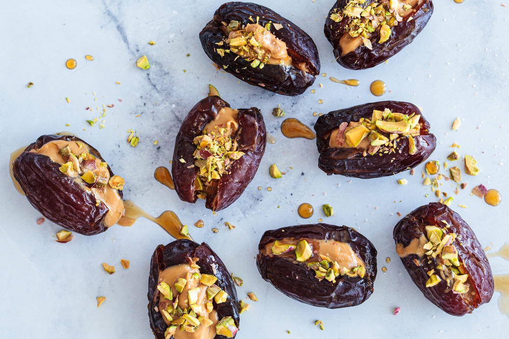 Dates stuffed with peanut butter and pistachios on a white marble background. Vegan dessert, healthy snack recipe.