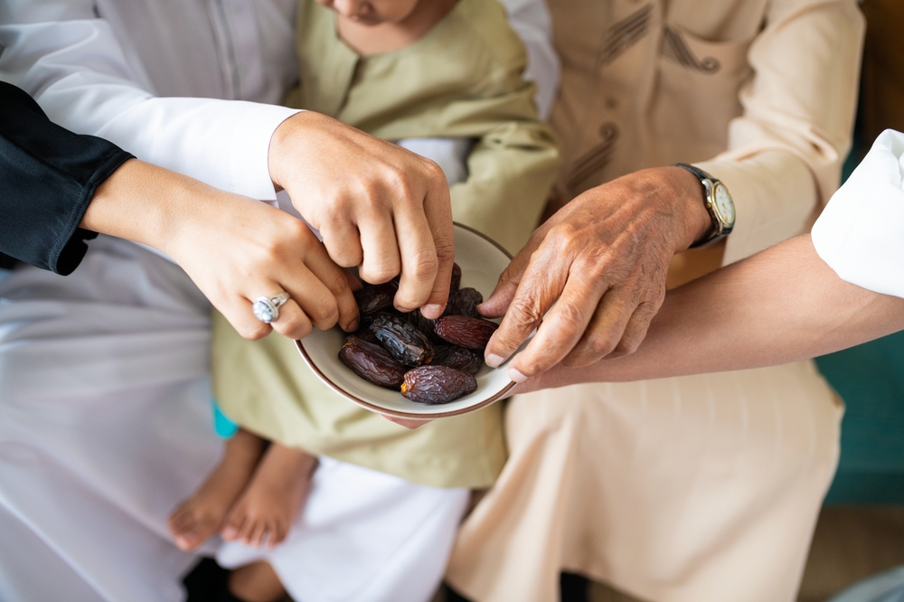 Hands reaching for dates in a bowl, symbolizing sharing and community. Diverse group sharing dates, highlighting cultural traditions and unity. People eating dates.
