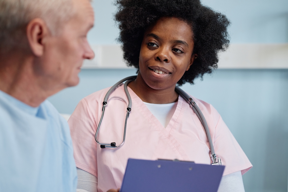 Nurse engaging with elderly patient, holding medical chart while showing friendly, attentive expression in hospital setting