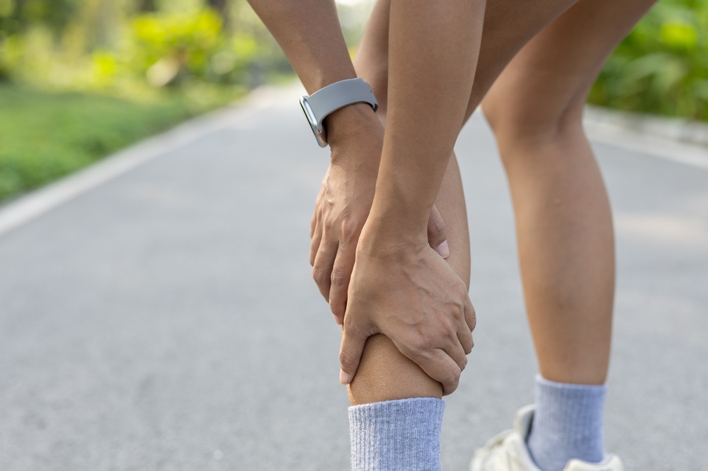 Close-up of women holding her lower leg in pain during outdoor workout. Muscle strain, shin splints, sports injury or cramp concept related to fitness, running, active lifestyle issues.
