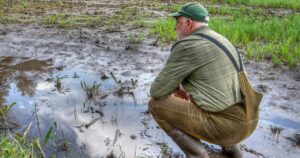 As the farmer surveys his flooded field, he feels a sense of despair. Climate change has brought more extreme weather, making it harder to grow crops and maintain his livelihood.